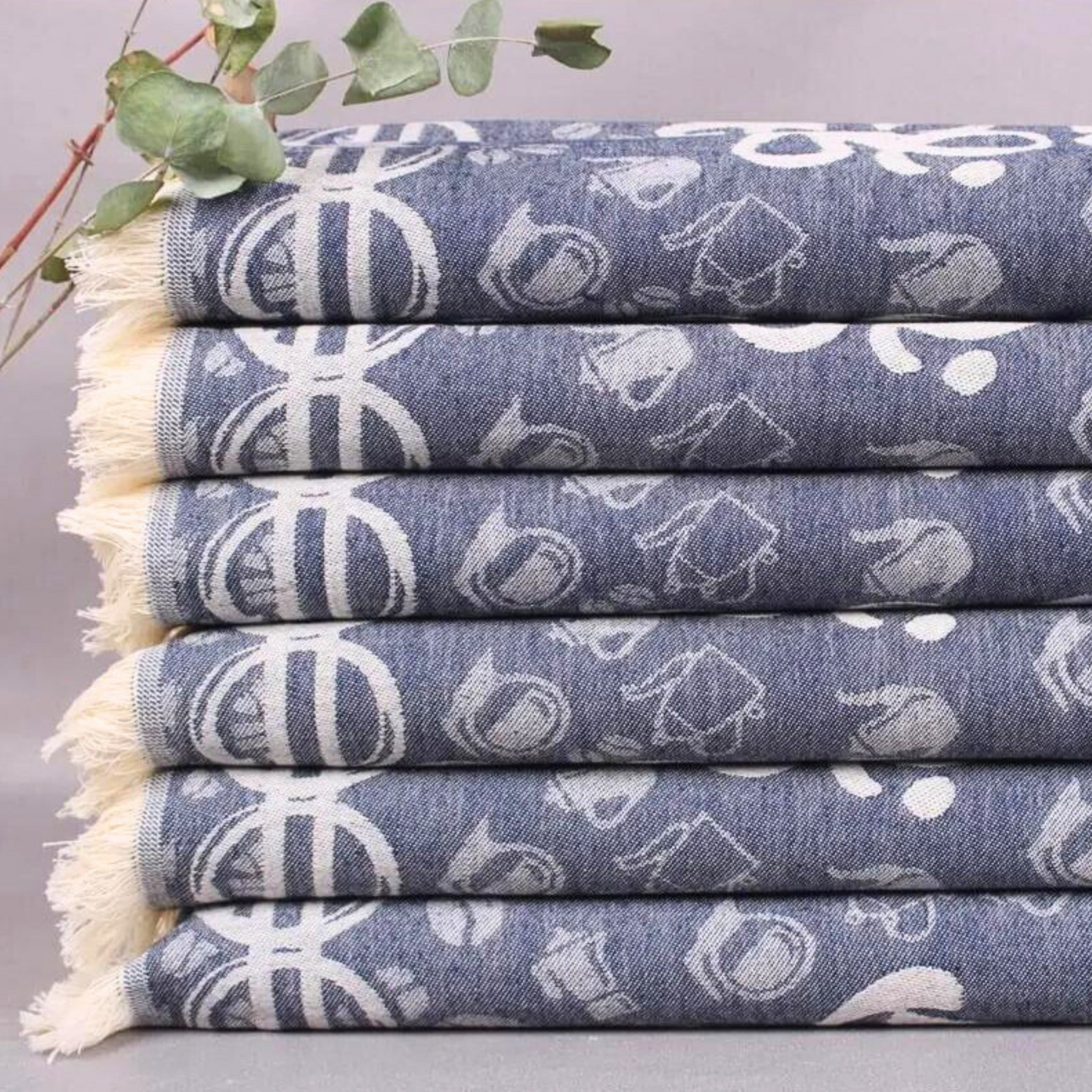 A stack of denim blue Turkish kitchen towels with white coffee and bean prints, finished with fringe edges.