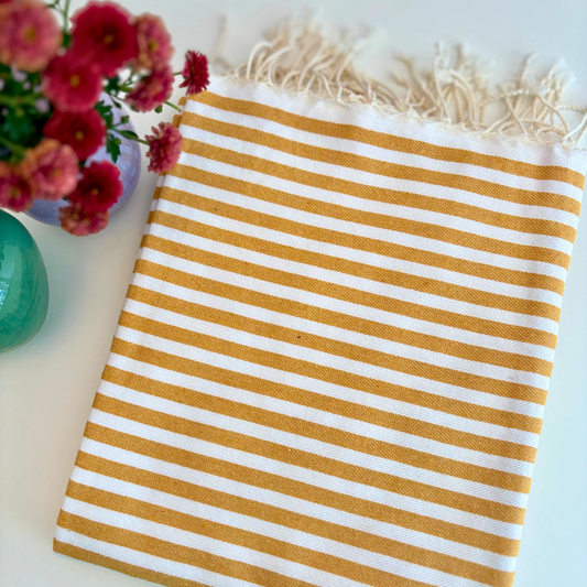 Mustard yellow Turkish towel with white stripes, featuring fun fringe details, perfect for adding vibrant color to home decor or outdoor and bathroom use.