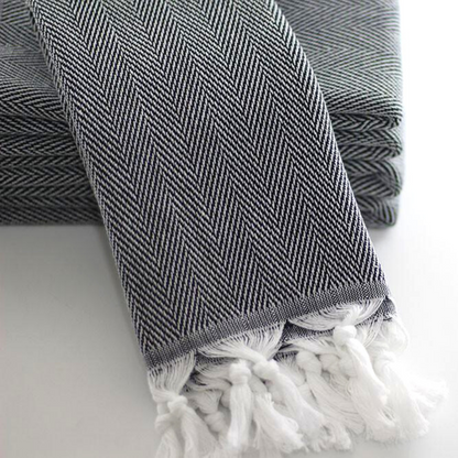 A close-up of a folded herringbone Turkish kitchen towel with intricate black and white zigzag patterns and white tassels at the edge, on a white surface