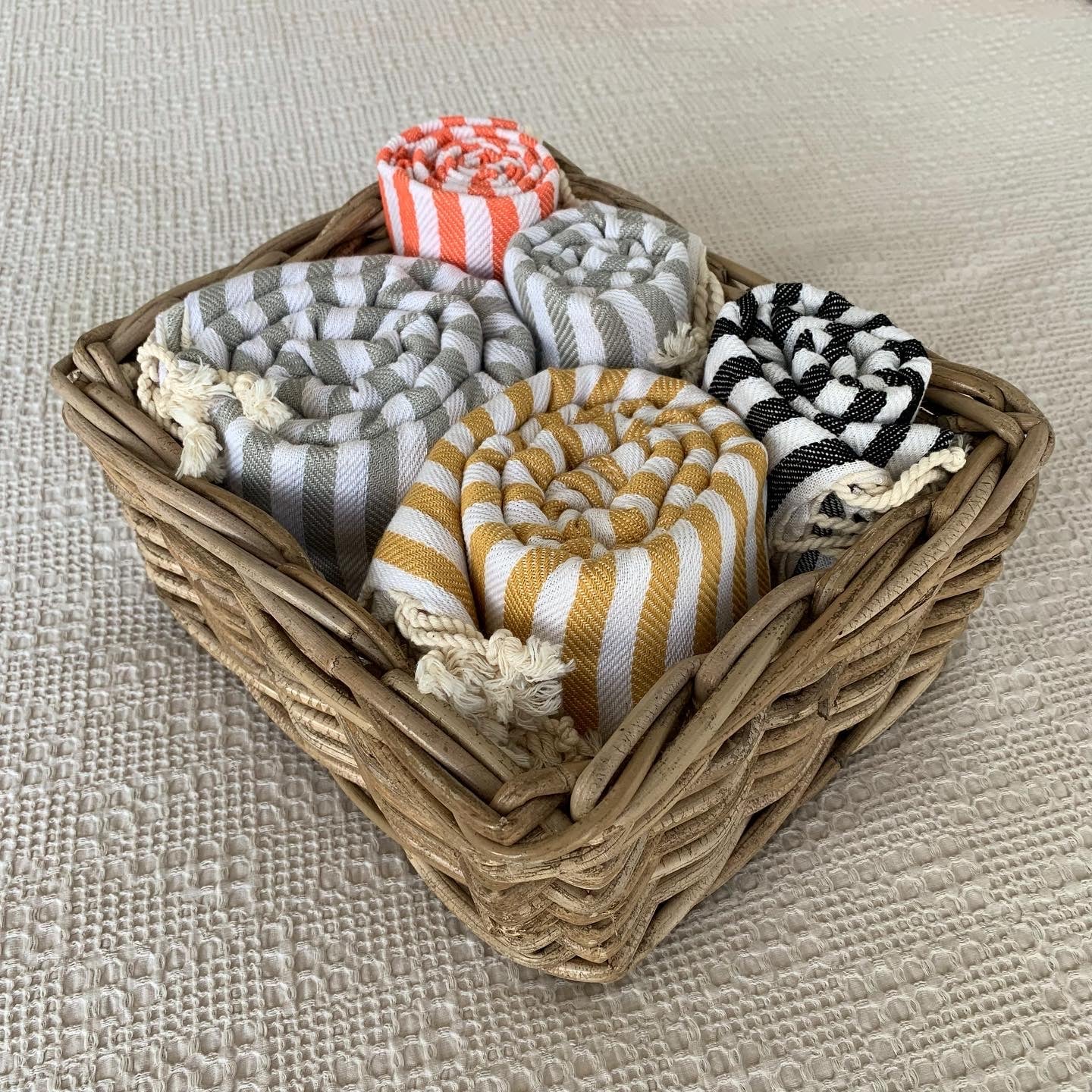 Set of Mediterranean Turkish towels in a basket, featuring striped patterns in various colours like mustard yellow, grey, black, and orange, perfect for versatile use in the bathroom, kitchen, or as decor.