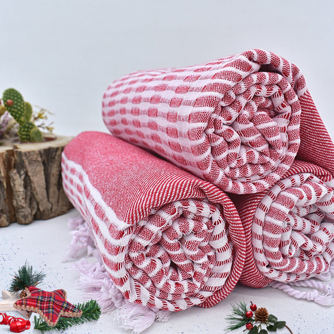 Rolled Turkish towels in red and white with intricate checkered and striped patterns, made from soft cotton, set on a festive background with holiday decor, perfect as holiday gifts