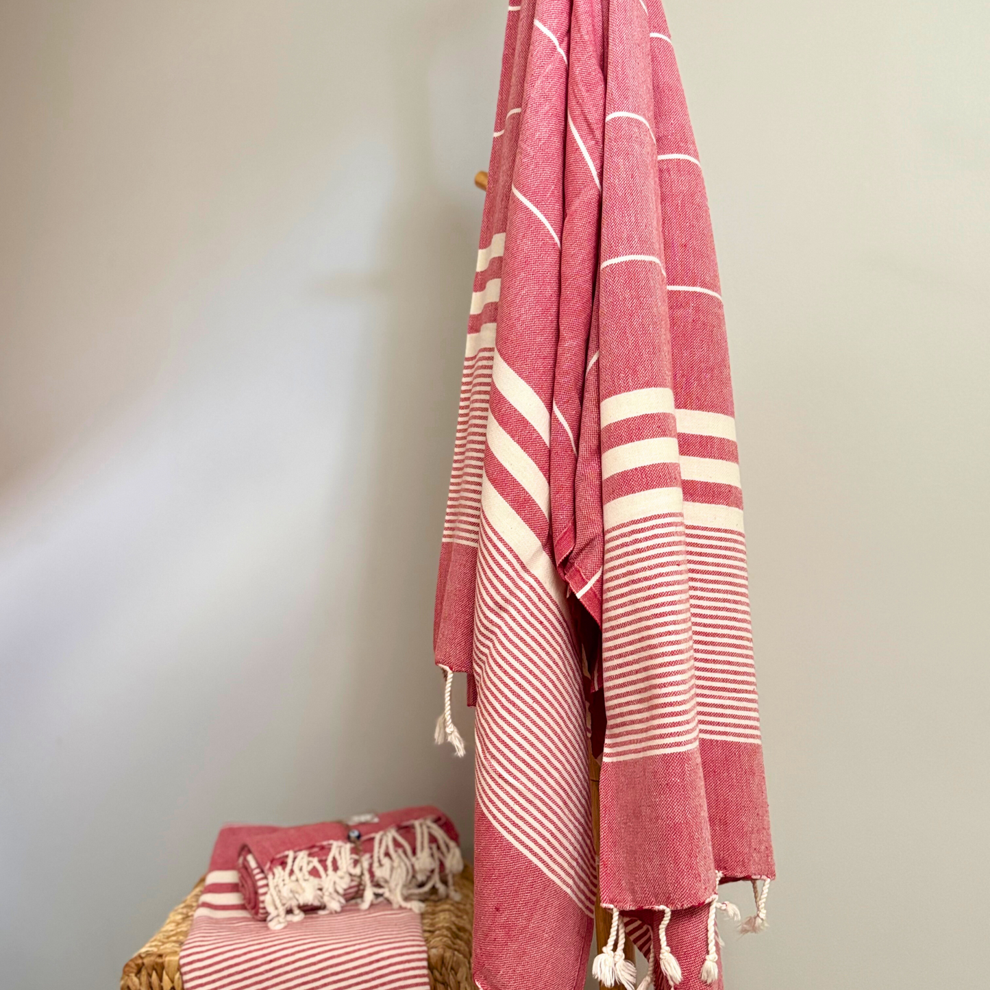 Red Turkish towel with cream stripes and fringed edges, hanging on a rack, ideal for stylish bath or home decor.