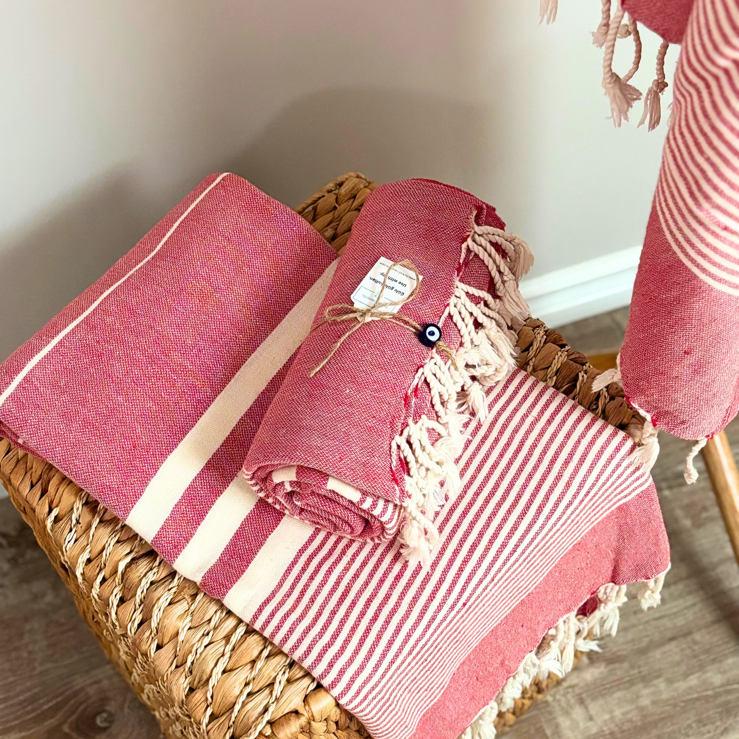 Folded red Turkish towels with cream stripes, tied with twine on a woven basket, perfect for home or bath use.