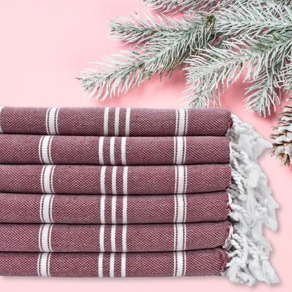 Burgundy Turkish kitchen towels with white stripes and fringe detail, stacked against a festive winter background with frosted pine branches, ideal for kitchen, bathroom, guest room.