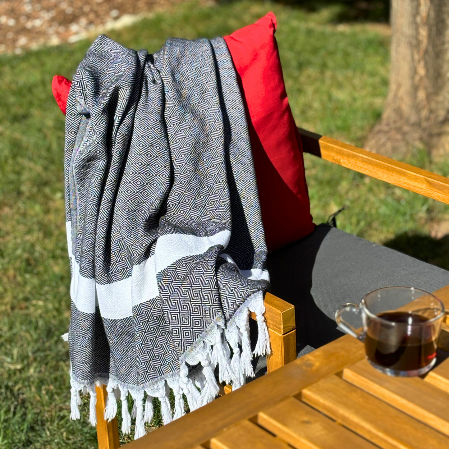 Black Sultan Turkish Towel draped over a wooden chair with red cushion, perfect for outdoor relaxation.