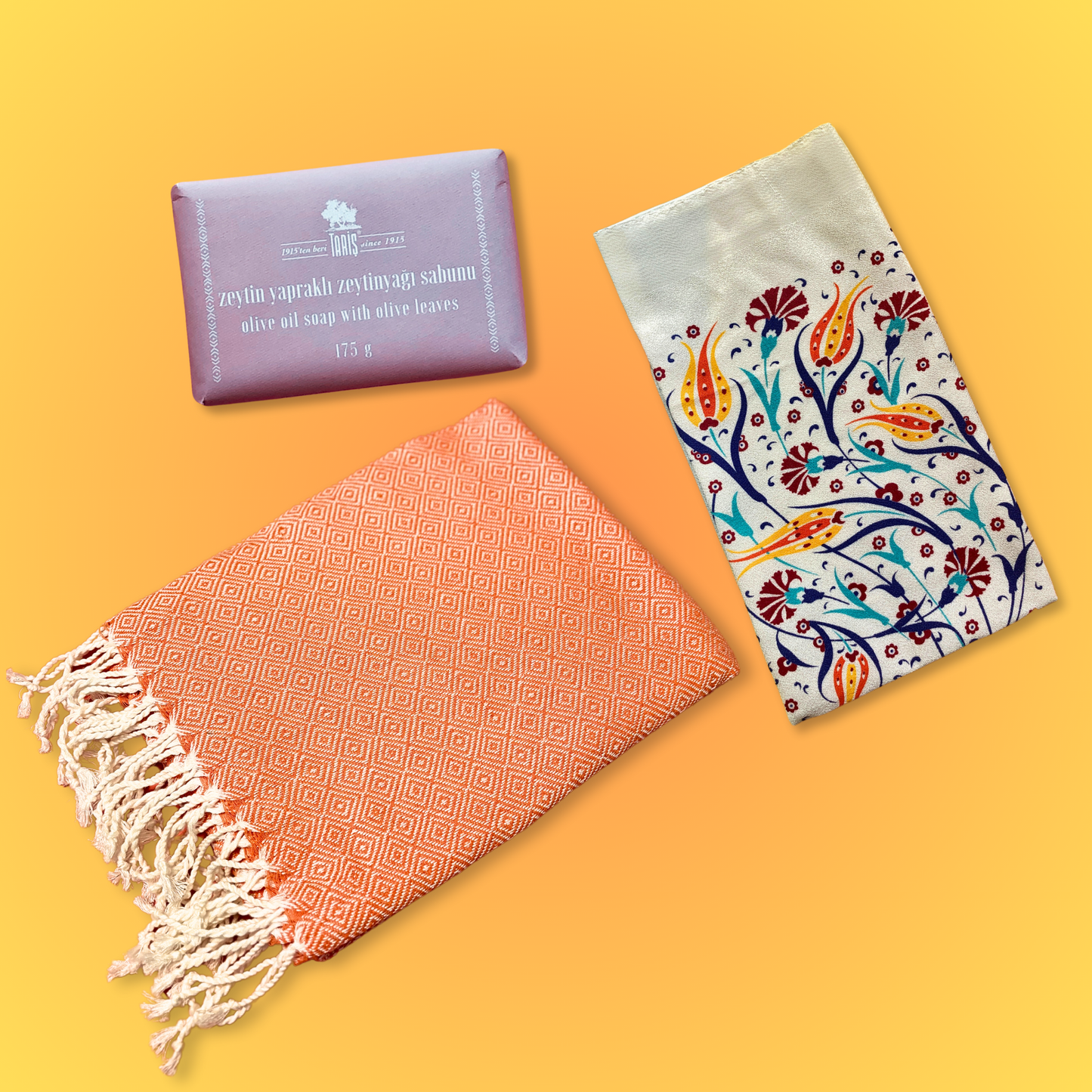 TULIP Turkish Bath Set with an orange Turkish towel, tulip-patterned exfoliating bath mitt, and olive oil soap with olive leaves on a orange-yellow background