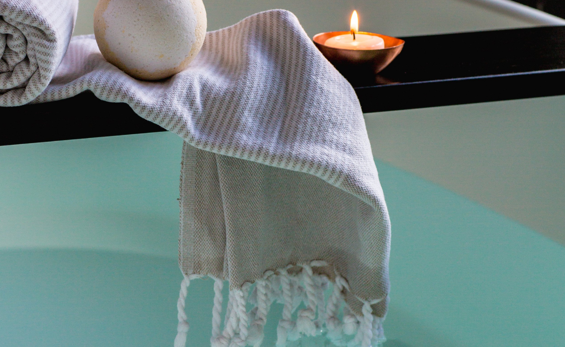Turkish towel with fringes over a bathtub with bath bomb and tealight candle