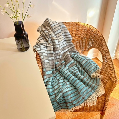 Blue WAVES Turkish Towel draped over a wicker chair next to a vase with white flowers.