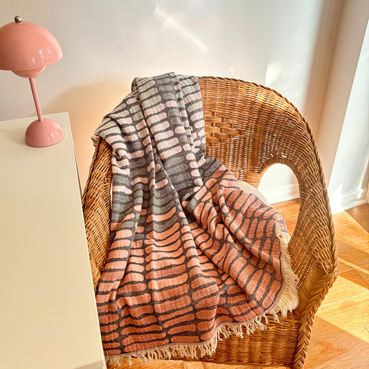 Pink WAVES Turkish Towel draped over a wicker chair next to a pink table lamp